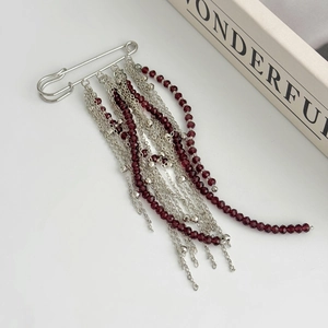 Détails d'une broche à franges argentées avec des perles rouge foncé et chaînes fines