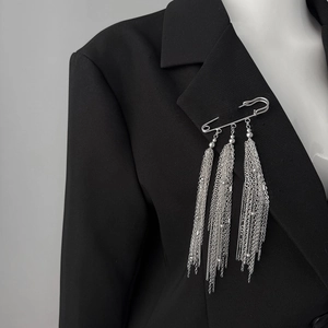 Detail of silver safety pin brooch with long layered metal chain tassels on a black blazer