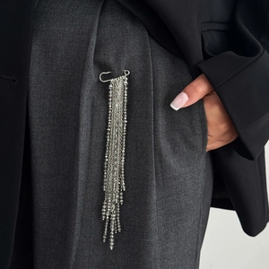 Close-up of a silver multi-layered chain brooch with grey crystal beads on dark suit pants