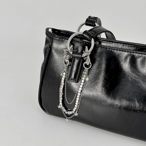 Detalle de bolso negro brillante con triple cadena plateada y colgantes de estrella modernos