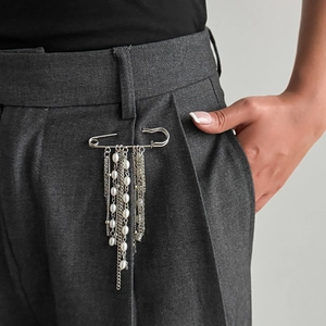 Dettaglio spilla argento con catenine e perle finte su pantaloni da abito grigio scuro