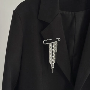 Dettaglio spilla a balia con nappe di perle applicata su un bavero di un blazer nero