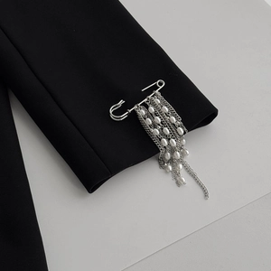 Detail of silver safety pin brooch with metallic fringe tassels and pearls on a blazer