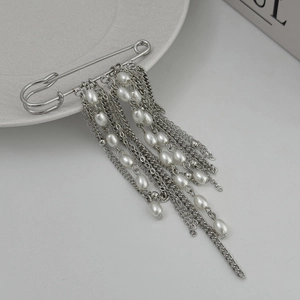 Detail of silver safety pin brooch featuring long metal tassels and white pearls