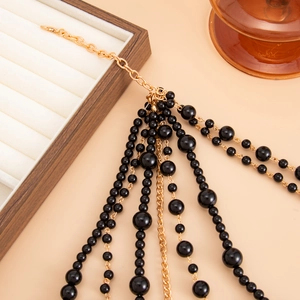 Detail of multilayer black bead necklace with gold tassels on a wooden jewelry tray