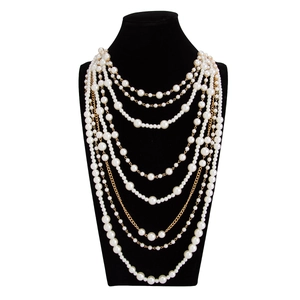 Detail of layered white imitation pearls and gold chain necklace on a black bust