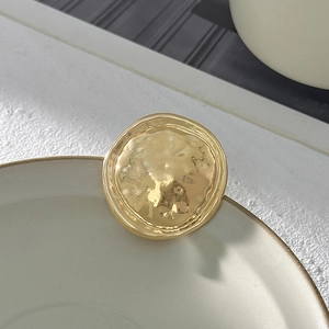 Dettaglio spilla rotonda dorata con trama martellata vintage sul bordo del piatto