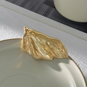 Dettaglio macro della spilla dorata irregolare con pieghe metalliche e effetto specchio