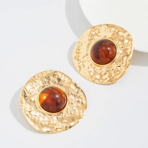 Macro detail of gold-tone hammer-textured round earrings with amber resin centers