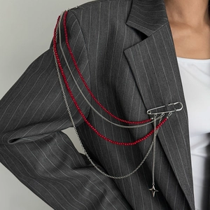 Détail de la broche d'épaule avec perles rouges, chaînes argentées et étoile sur veste