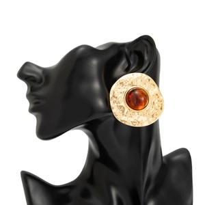 Macro detail of round hammered gold metal earring with amber resin gemstone on black bust