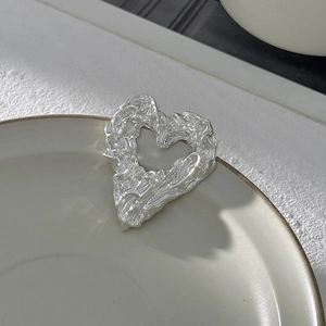 Dettaglio macro di spilla a cuore in argento con trama lavica fluida su piatto bianco