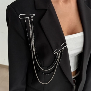 Détail d'une broche étoile argentée avec chaînes de perles noires sur un blazer de costume