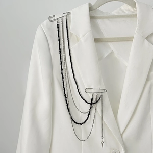 Détail de la longue chaîne argentée et broche à pompons noirs sur une veste blanche