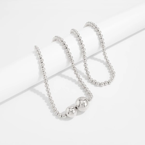 Detail van zilveren kralenketting gedrapeerd over witte geometrische rekwisieten