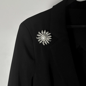 Dettaglio della spilla a fiore argento con cristalli e perla su un blazer nero elegante