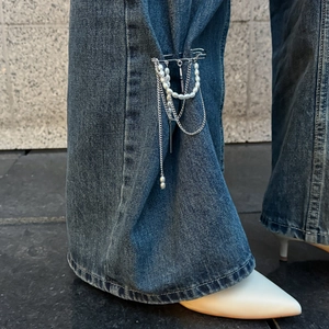 Detail of silver pearl brooch with tassels pinned to the side of dark blue denim jeans