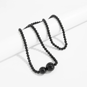 Detail van een gelaagde zwarte kralenketting met gepolijste grote bolvormige hangers