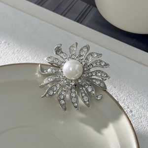 Dettaglio di una spilla a fiore argento con grande perla bianca e strass scintillanti