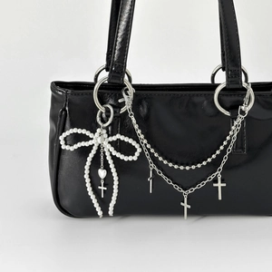 Chic black leather bag with pearl bow, silver chains, and metallic cross pendant