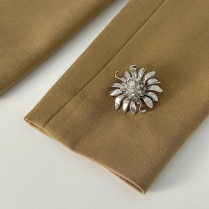 Dettaglio di una spilla floreale argento con cristalli su una giacca color kaki