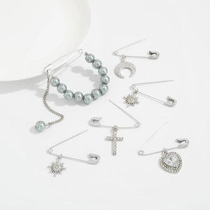 Detail of silver safety pin brooches featuring pearl, moon, and cross pendants