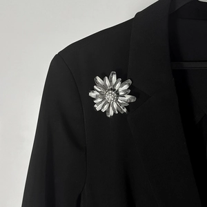 Dettaglio di una spilla a fiore argento con cristalli sul bavero di una giacca nera