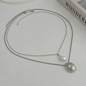 Detailed close-up of double-layer silver necklaces with baroque pearl and bean pendants