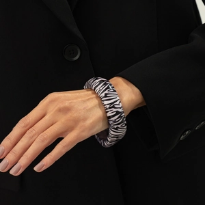 Détail d'un large bracelet en résine à motif zèbre porté par un mannequin sur un costume