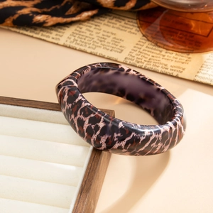 Gros plan d'un large bracelet en résine à motif léopard posé sur une boîte à bijoux blanche