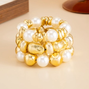 Detailed view of layered elastic bracelets with white pearls and hammered gold beads