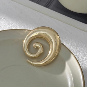 Dettaglio macro della spilla dorata a spirale con pieghe liquide e texture lucida