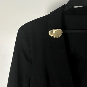 Dettaglio di una spilla in metallo dorato fluido irregolare su un risvolto di blazer nero
