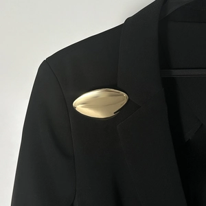 Dettaglio di una spilla in metallo dorato lucido fissata sul risvolto di un blazer nero