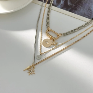 Detailed close-up of layered mixed-metal necklaces with star and eye charms on white stone