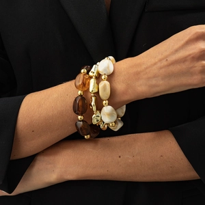 Close-up of stacked beaded elastic bracelets in amber, gold, and cream marble resin