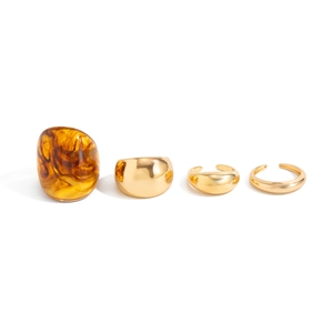 Set of four gold polished metal rings with an amber resin wide band on white background
