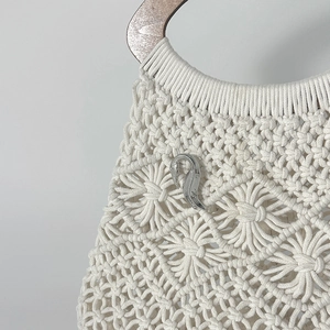 Dettaglio spilla a cigno su borsa in macramè crema con motivo floreale intrecciato