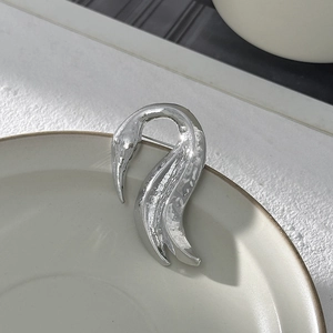 Dettaglio macro della spilla a cigno in argento con trama martellata su piatto in ceramica
