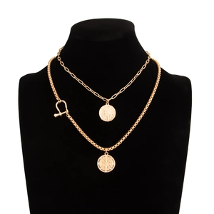 Detail of layered gold hip-hop necklace with coin and compass star pendants on a black bust