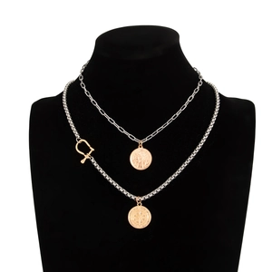 Detail of layered gold and silver chains featuring a coin and compass pendant