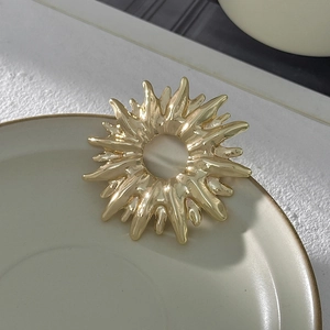 Dettaglio di una spilla in metallo dorato a raggiera con texture fluida e design moderno