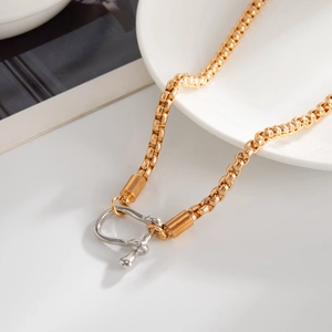 Close-up of a two-tone gold chain necklace featuring a polished silver U-shape horseshoe link