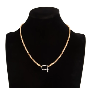 Detailed view of golden snake chain necklace with U-shaped buckle on black velvet display