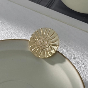 Vista macro di una spilla a sole dorata con texture a rilievo su ceramica bianca