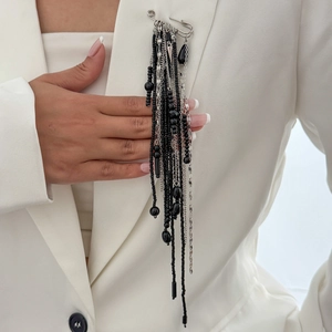 Détail d'une longue broche à pompons noirs épinglée sur une veste de costume blanche