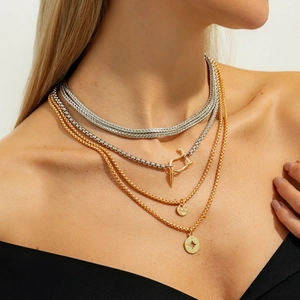Detail of layered gold and silver chains featuring compass and spike pendants on model