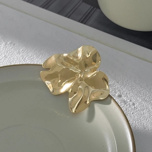 Dettaglio di una clip a fiore dorata irregolare pieghettata su piatto ceramica