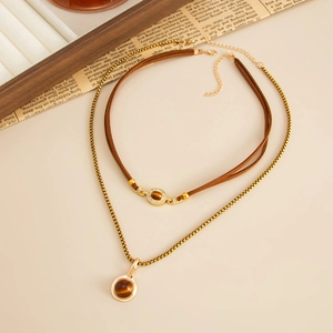 Detail van gelaagde gouden kettingen met bruine tijgeroog hangers op koord en metalen ketting