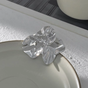 Dettaglio della spilla a fiore argento con pieghe metalliche irregolari e finitura lucida